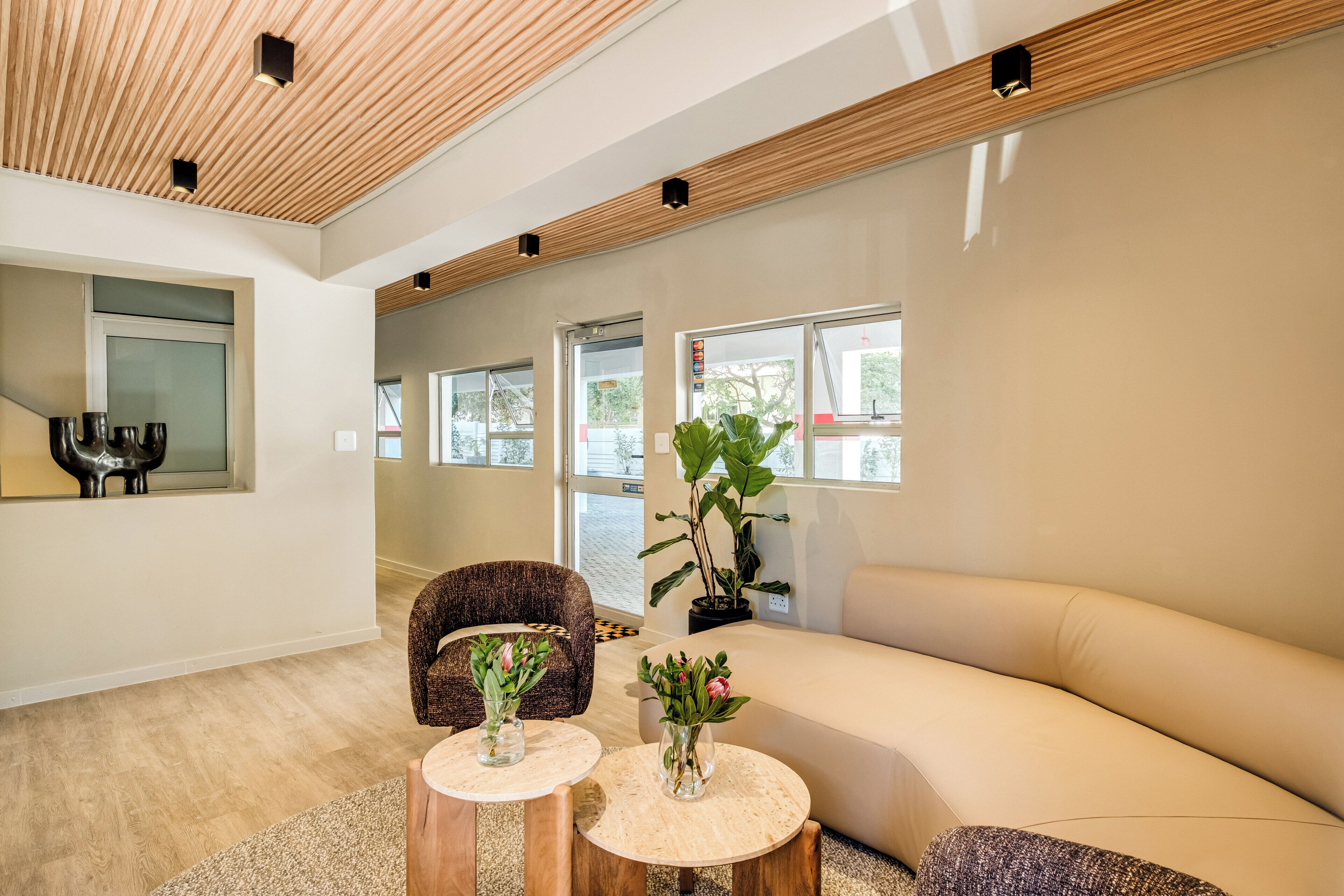 Un interior moderno con techo de madera, un sofá, dos mesas redondas con jarrones y una silla.