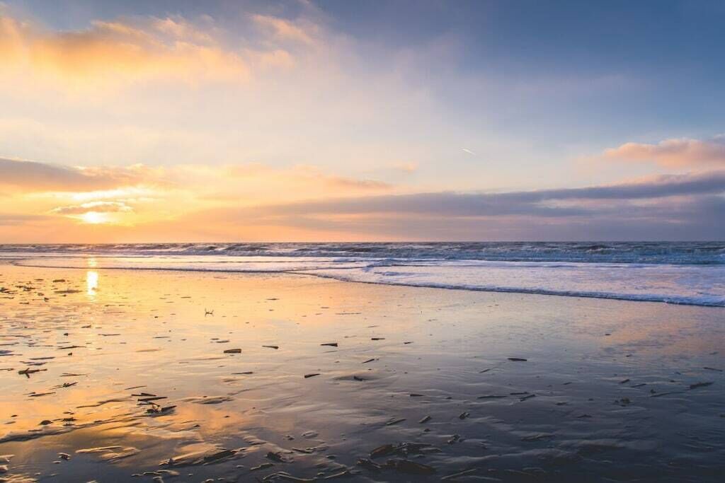 Uma praia com pôr do sol, ondas e pegadas na areia.