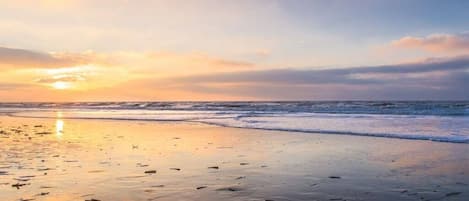 Uma praia com pôr do sol, ondas e pegadas na areia.