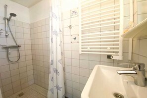 Un baño con ducha, lavamanos y toallero.