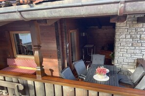 Une terrasse extérieure avec une table et des chaises en bois, un mur en pierre et une fenêtre.