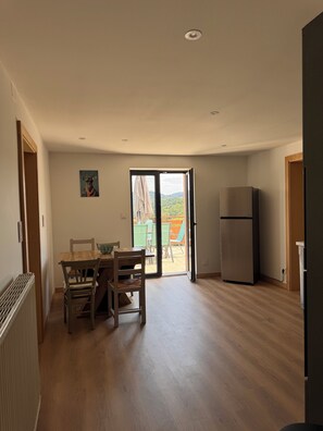 A spacious room with a wooden floor, a dining table with chairs, a refrigerator, and a sliding glass door leading to an outdoor area with chairs and a table. - House for 6 people Saint-Nabord (Saint-Nabord)