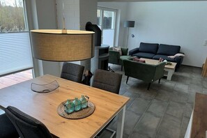 Een moderne woonkamer met een eettafel, stoelen, een bank en een lamp.