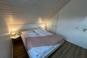 Een eenpersoonsbed met hoofdeinde, een nachtkastje met een lamp en een deur aan de rechterkant.