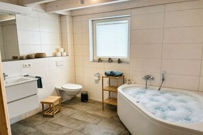 Een moderne badkamer met een bad, toilet, wastafel en een raam met zonwering.
