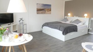 Ein modernes Schlafzimmer mit einem Bett, Nachttischlampen, einem Fernseher, einem Tisch mit Frühstücksangeboten und einem Gemälde an der Wand.