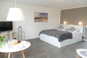 Camera da letto moderna con un letto, lampade da comodino, una televisione, un tavolo imbandito per la colazione e un quadro appeso al muro.