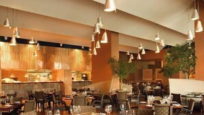 Ein Restaurant mit mehreren Tischen und Stühlen, hängenden Pendelleuchten und einer Wand mit Holzverkleidung.