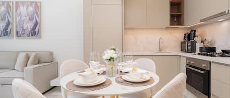 A modern kitchen with a dining area, featuring a round table with chairs, a sofa, and artwork on the wall.