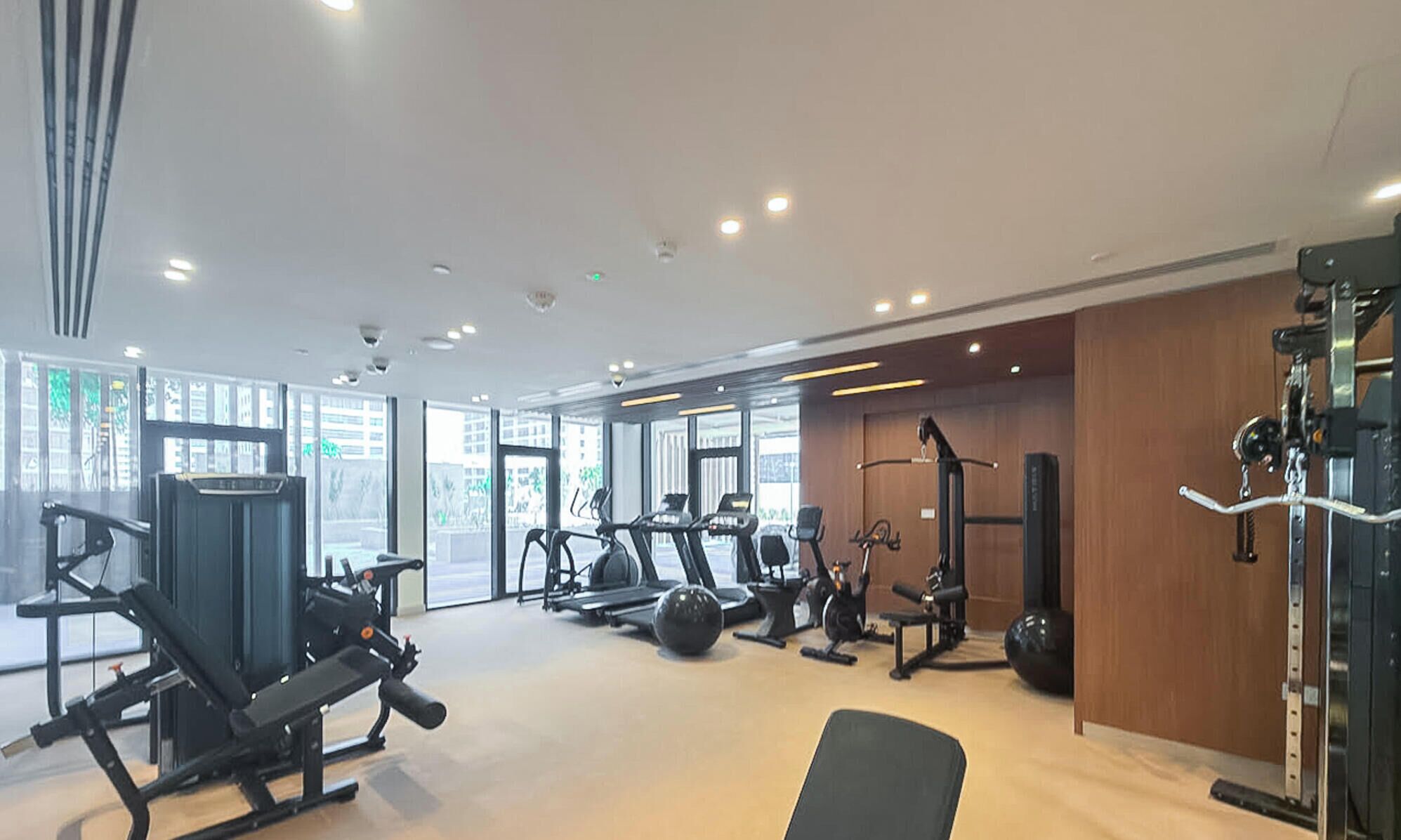 A modern gym with various exercise equipment, large windows, and a clean, well-lit interior.