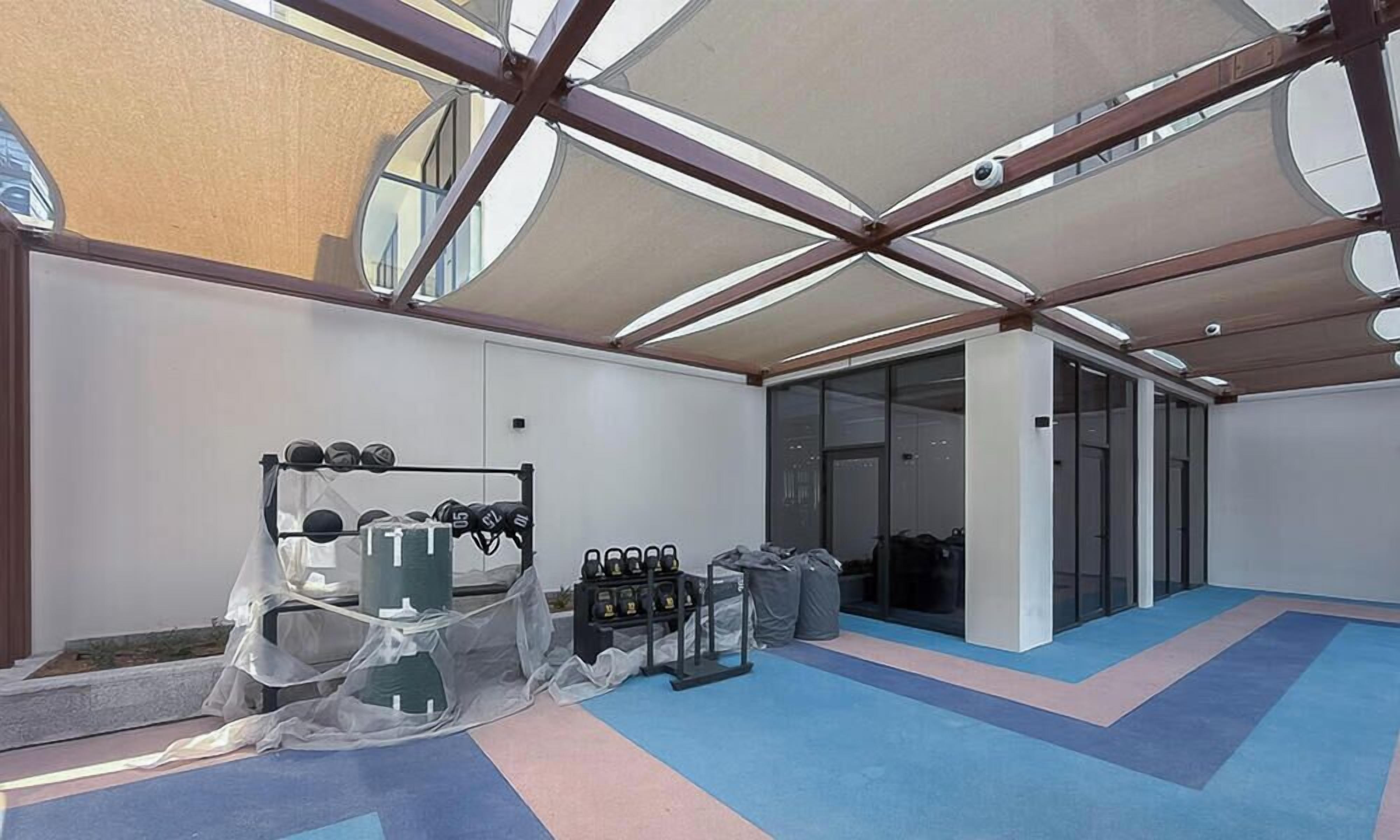 An outdoor gym area with exercise equipment, a covered seating area, and a view of the city through large windows.