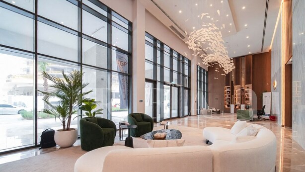 Um hall amplo com grandes janelas, um sofá branco arredondado e um lustre moderno.