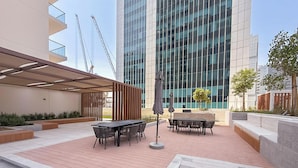 Área de pátio externo com mesa e cadeiras, pérgola e um edifício moderno ao fundo.