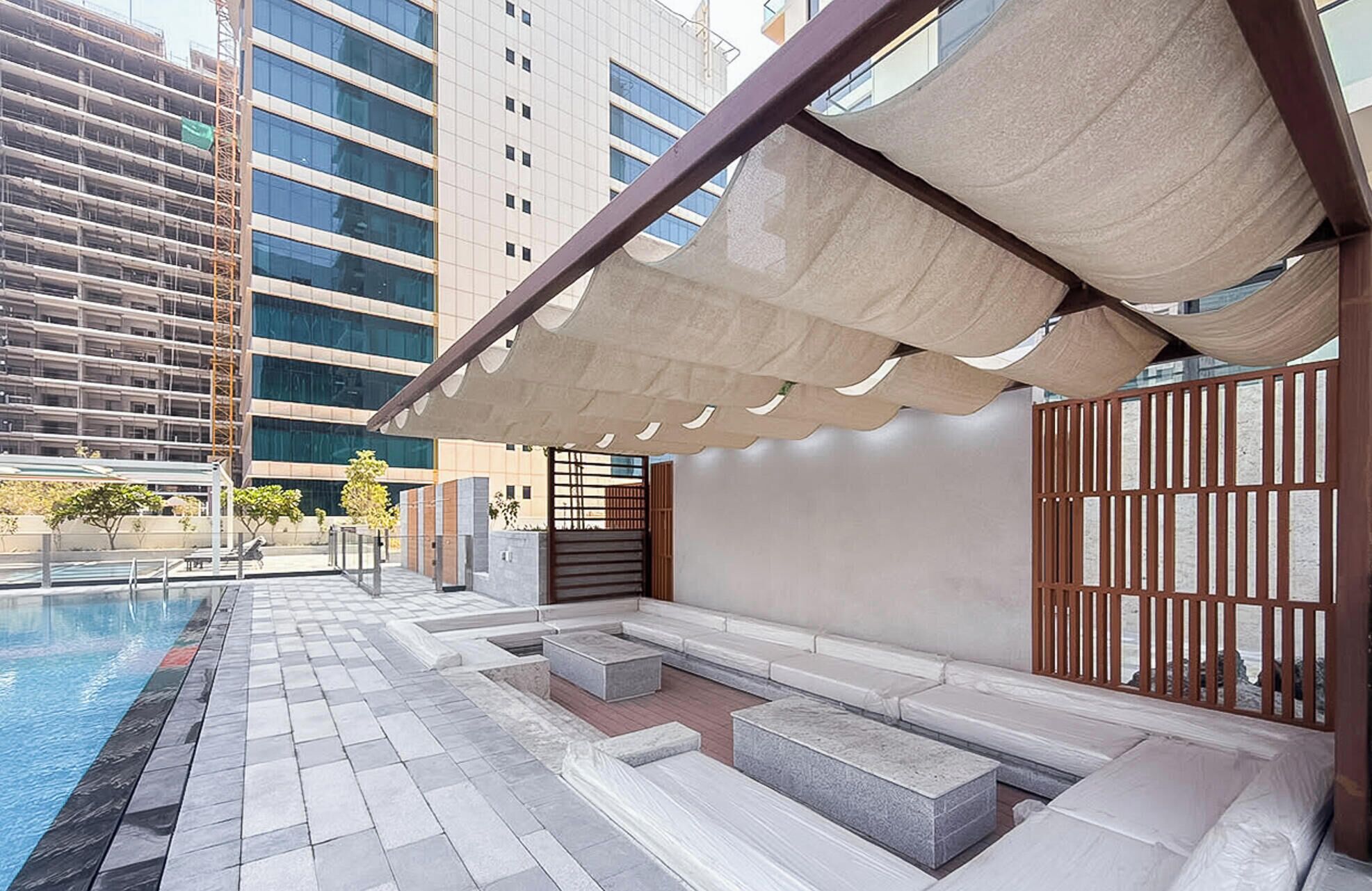 A poolside area with a covered seating area, steps leading to a pool, and a view of modern buildings in the background.