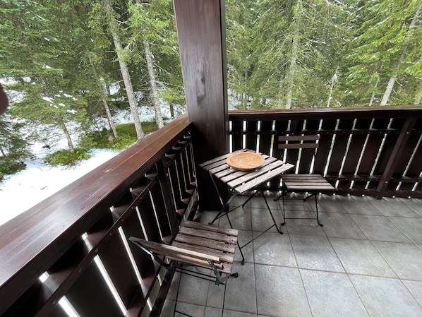 Una terraza de madera con una mesa y sillas, con vista a una zona boscosa.
