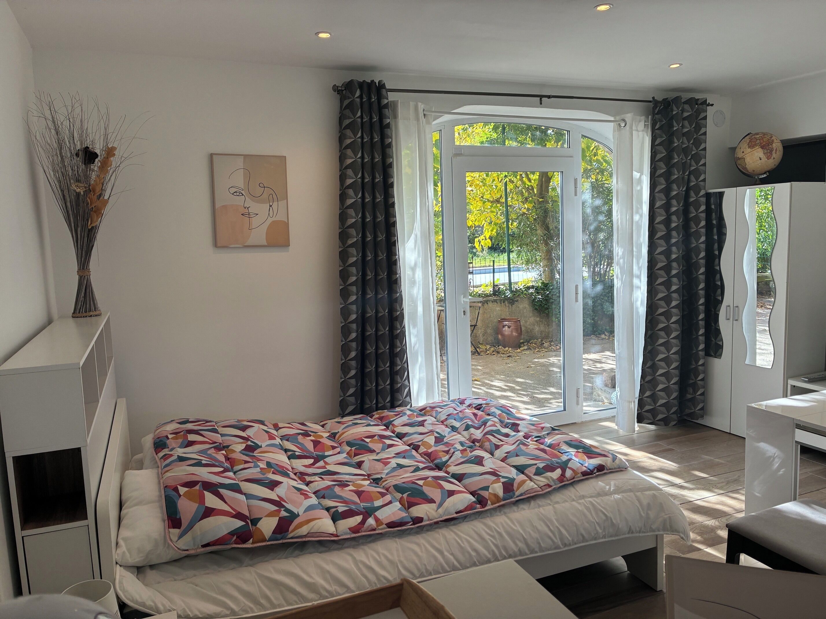 Un dormitorio con cama, mesita de noche, cómoda, ventana con cortinas y un globo terráqueo colgado en la pared.