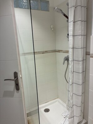 Eine Dusche mit Glastür, Brausekopf und Duschvorhang.