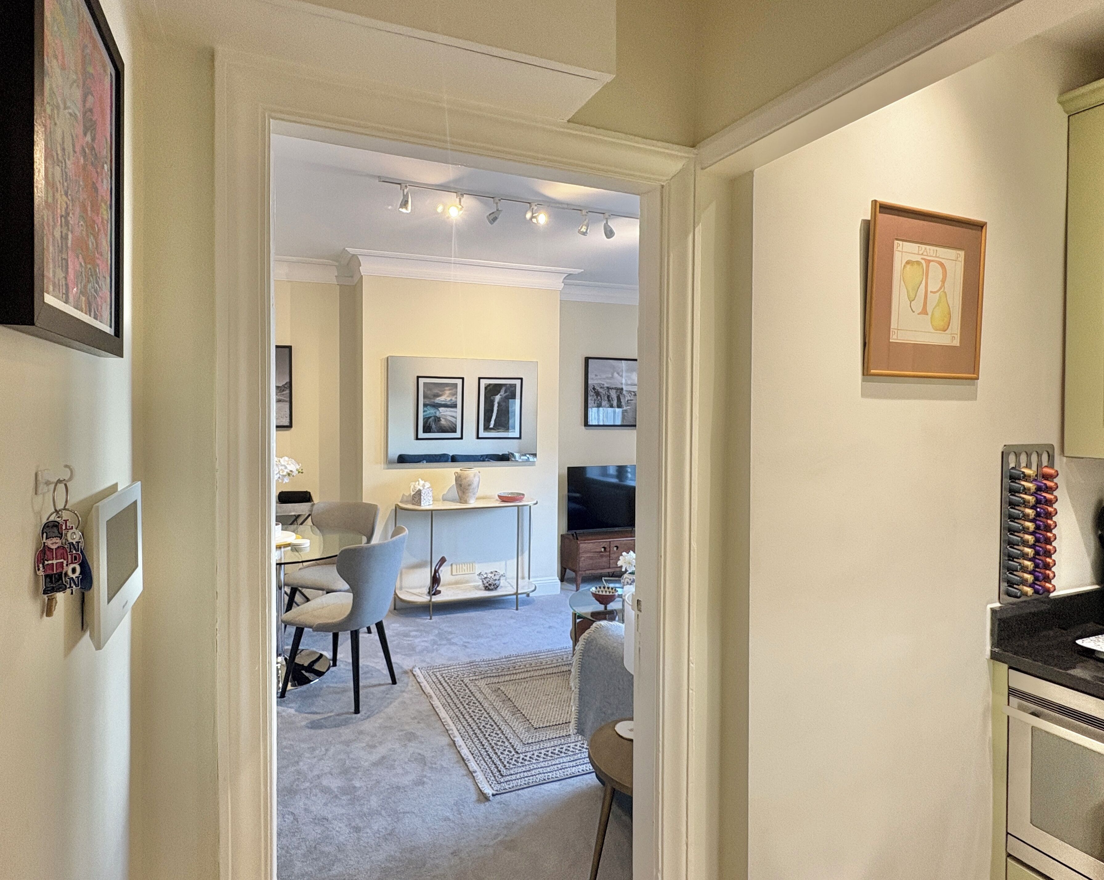A modern kitchen with a built-in oven, a dining area with a table and chairs, and a living room with a TV and framed artwork.