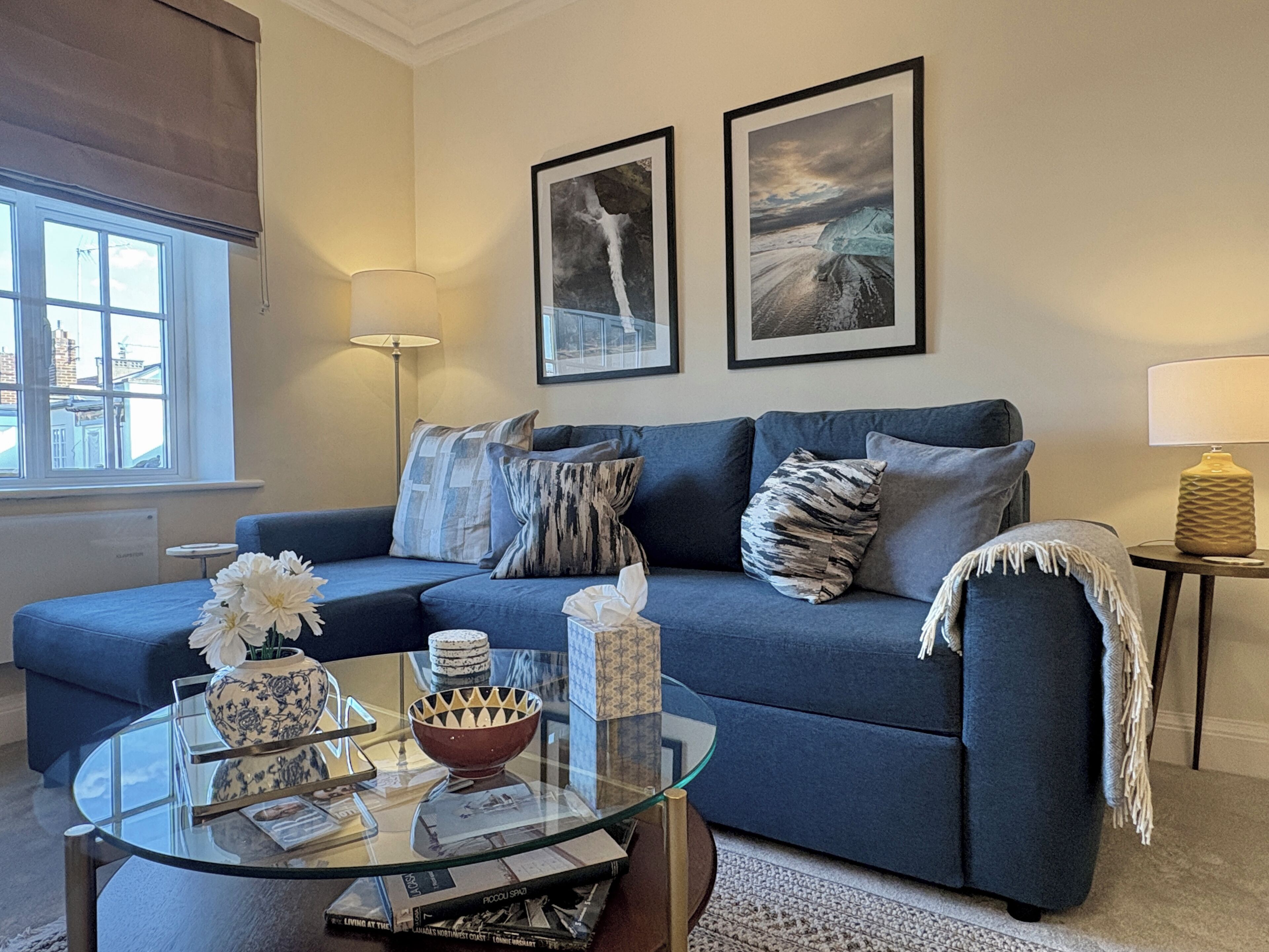 A living room with a blue sofa, a glass coffee table, and two framed pictures on the wall.