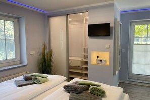 Ein Hotelzimmer mit zwei Betten, einem an der Wand befestigten Fernseher, einem Schiebetürenschrank und einem Fenster mit Jalousien.