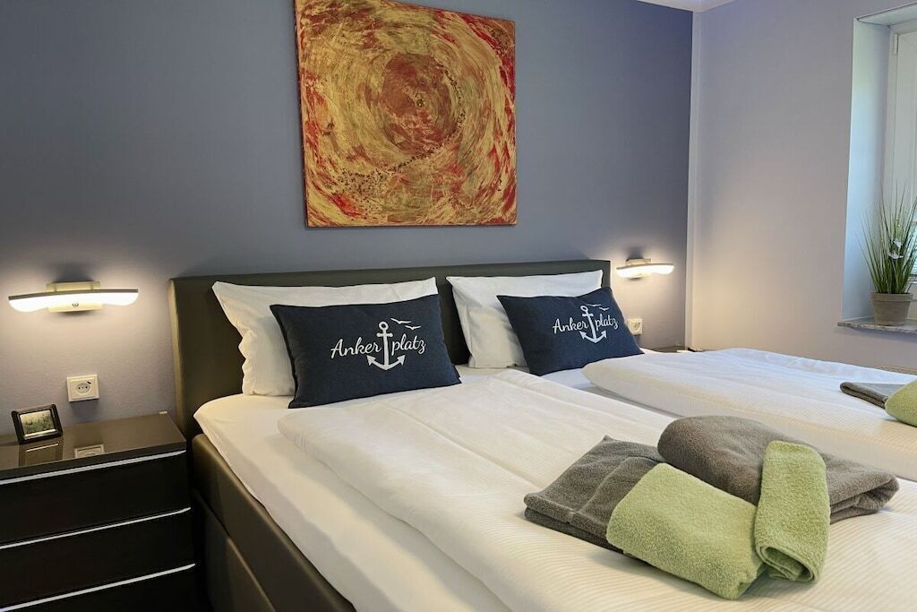 Et hotelværelse med to senge, hver med en pude med hotellets logo, et stort abstrakt maleri på væggen og et natbord med en lampe.