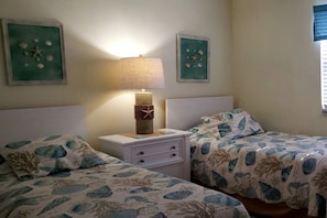 A room with two beds, each with a sea-themed bedspread, a nightstand with a lamp, and wall art depicting sea creatures. - Holiday home with 2 bedrooms (St. Augustine)