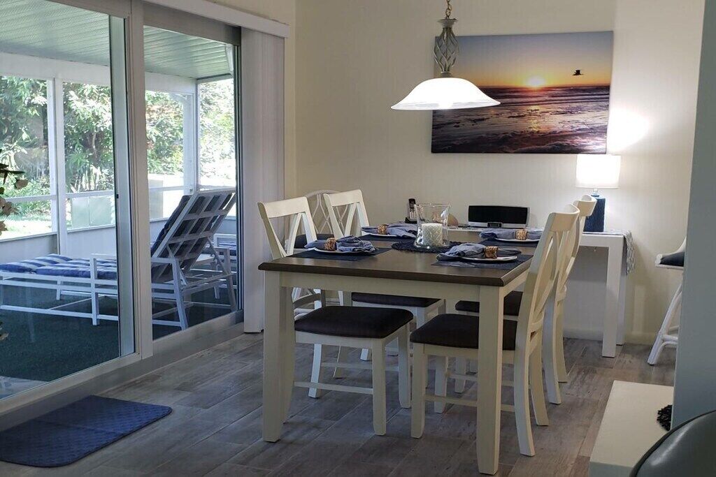 A dining area with a table, chairs, a lamp, and a painting of a sunset.