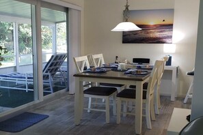 A dining area with a table, chairs, a lamp, and a painting of a sunset. - Holiday home with 2 bedrooms (St. Augustine)