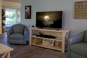 A living room with a television on a stand, a chair, a small table, and a window with a view of greenery. - Holiday home with 2 bedrooms (St. Augustine)
