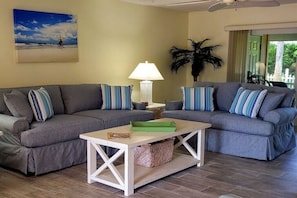 A living room with two grey sofas, striped pillows, a white coffee table, a lamp, and a painting of a beach scene. - Holiday home with 2 bedrooms (St. Augustine)