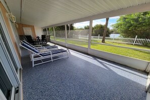 A covered outdoor area with lounge chairs and a table, large windows with a view of a grassy area and a fence. - Holiday home with 2 bedrooms (St. Augustine)