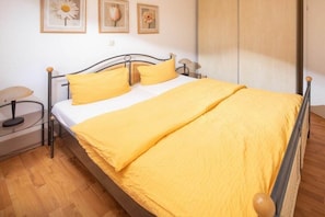 A bed with a metal frame, a wooden headboard, and a yellow bedspread. - Cloverleaf in the Sanderling house (Juist)