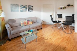 A living room with a sofa, a glass coffee table, and a dining area with a table and chairs. - Cloverleaf in the Sanderling house (Juist)