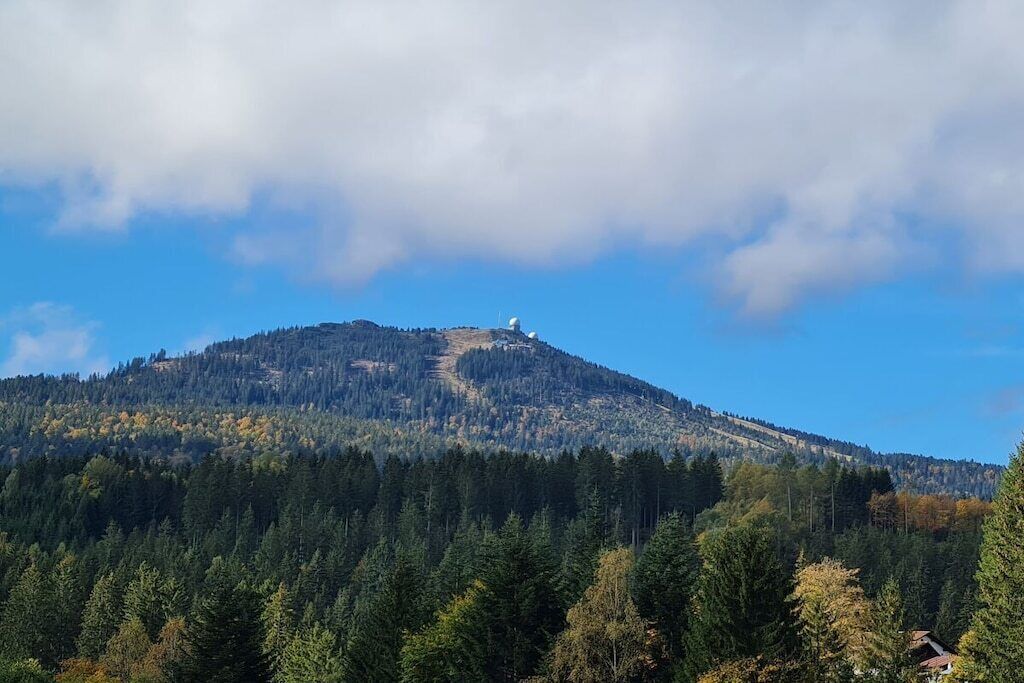 Une montagne surmontée d’un petit bâtiment, entourée d’une forêt dense.