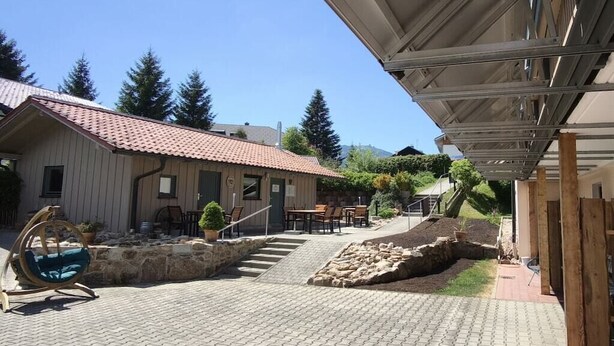 A building with a tiled roof, outdoor seating, and a stone retaining wall. - Holiday apartment with 1 bedroom (Bayerisch Eisenstein)