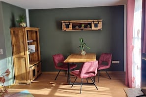 Ein Zimmer mit einem Holzesstisch, zwei rosafarbenen Stühlen, einem Holzschrank und einem Regal mit Pflanzen.