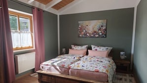 A bedroom with a wooden bed frame, floral bedding, a radiator, a window with curtains, and a painting on the wall. - Holiday apartment with 1 bedroom (Bayerisch Eisenstein)
