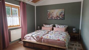 Ein Schlafzimmer mit hölzernem Bettgestell, floralem Bettbezug, einem Heizkörper, einem Fenster mit Vorhängen und einem Bild an der Wand.