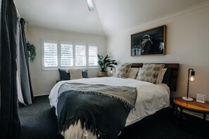 Een slaapkamer met een groot bed, een nachtkastje, een lamp, een potplant en een schilderij aan de muur.