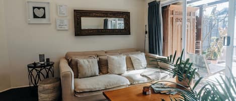 A living room with a beige sofa, a coffee table, a mirror, and a window with curtains.