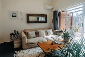 Ein Wohnzimmer mit einem beigen Sofa, einem Couchtisch, einem Spiegel und einem Fenster mit Vorhängen.