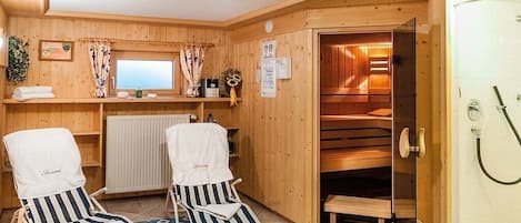 A sauna room with two striped lounge chairs, a wooden bench, and a glass door leading to a steam room.
