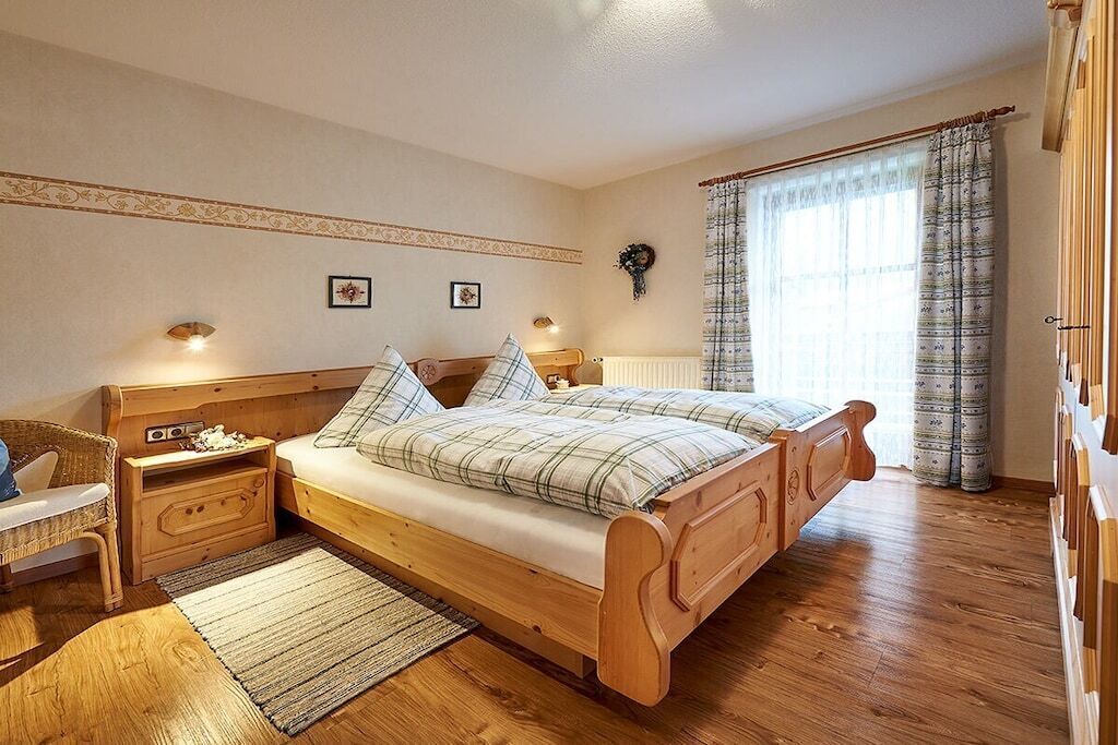 Un dormitorio con una cama de madera, mesitas de noche, una silla de mimbre y una ventana con cortinas.
