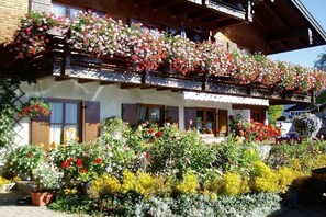 A building with a balcony covered in flowers, a front entrance, and a garden with various plants.