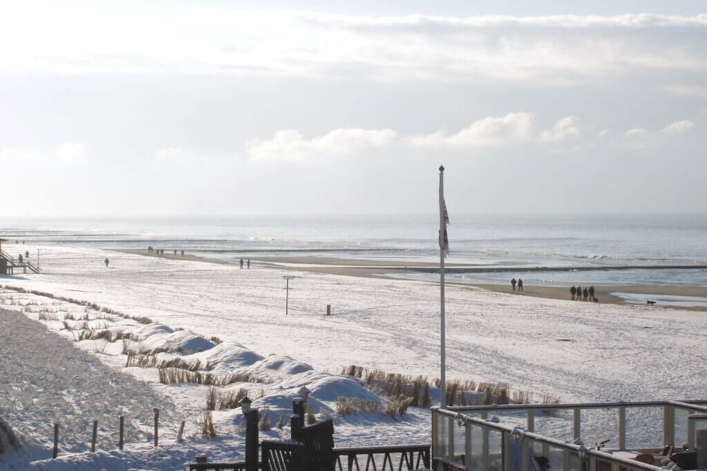 Una playa nevada con un paseo marítimo, un asta de bandera y vistas al mar.