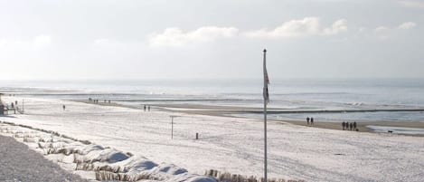 A snow-covered beach with a boardwalk, a flagpole, and a view of the sea.
