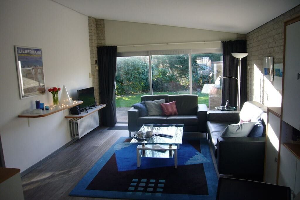 Un salon moderne avec un canapé, une table basse et un téléviseur. Une grande fenêtre offre une vue sur l’extérieur.
