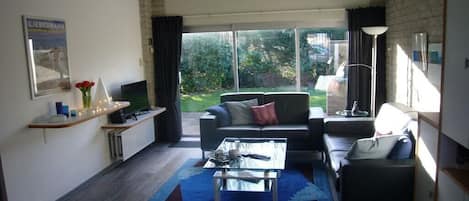 A modern living room with a sofa, a coffee table, and a television. There is a large window providing a view of the outdoors.