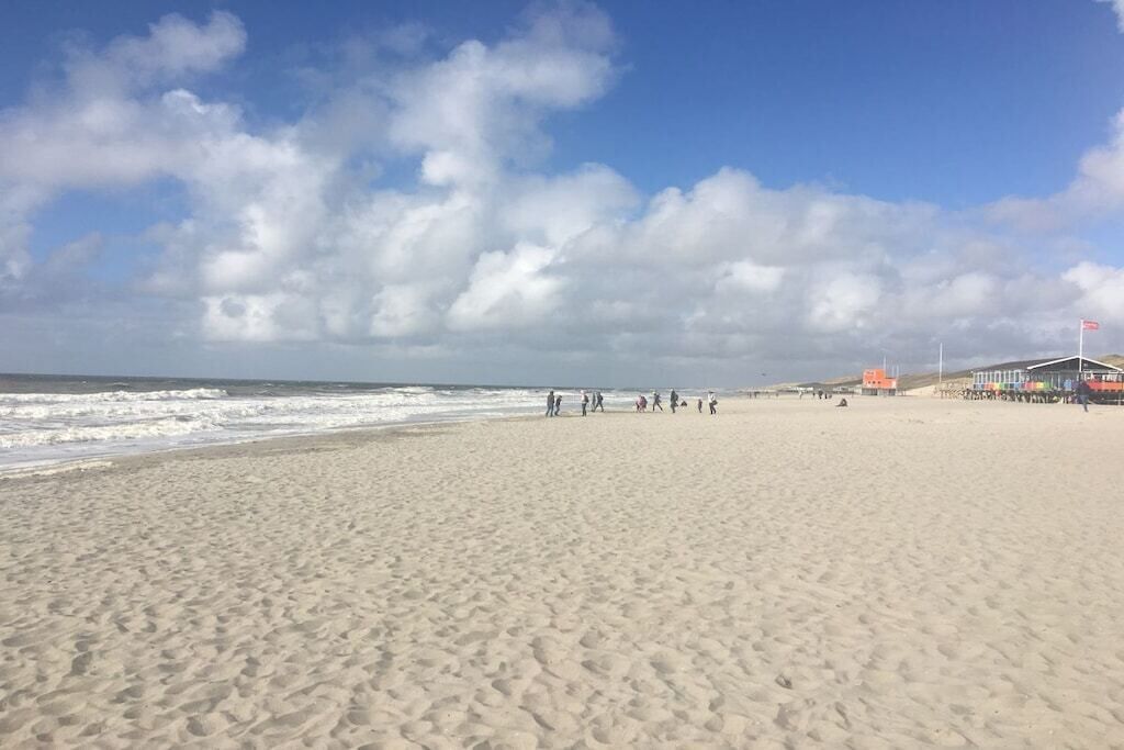 A sandy beach with footprints, a clear sky, and a few people in the distance.