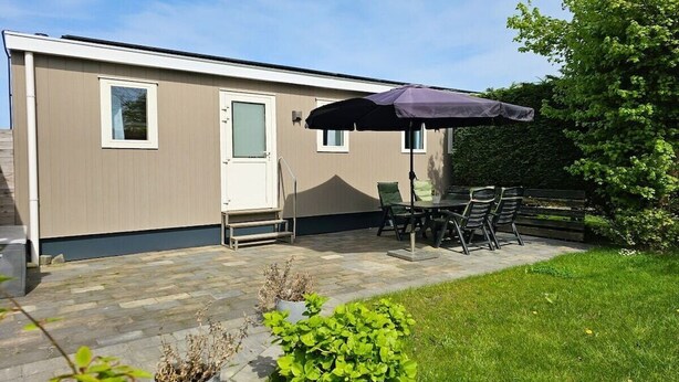 A mobile home with a patio area featuring a table and chairs, a door, and a window. - OK40 Chalet Oostkapelle (Oostkapelle)
